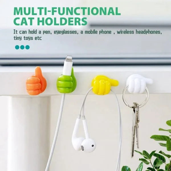 Four colorful cat-shaped wall hooks in orange, green, yellow, and white are shown mounted on a white surface, each holding a different item: a pen, a white phone cable, white earbuds, and keys. Text at the top reads 'MULTI-FUNCTIONAL CAT HOLDERS' with a description of uses.