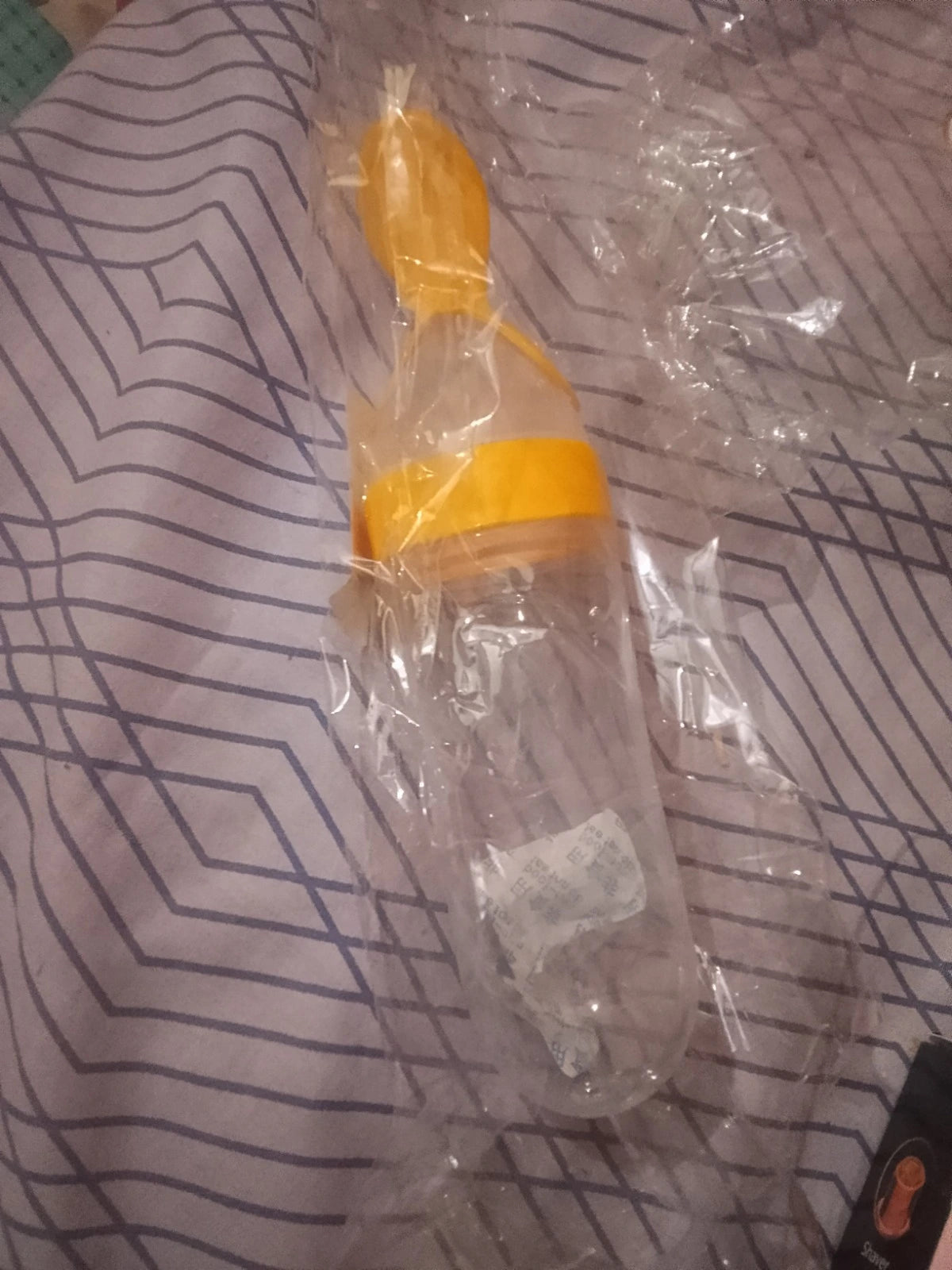 Orange and clear plastic bottle with a nozzle on a patterned fabric background