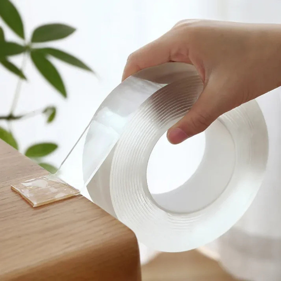 Hand holding a roll of clear tape with a blurred green plant in the background