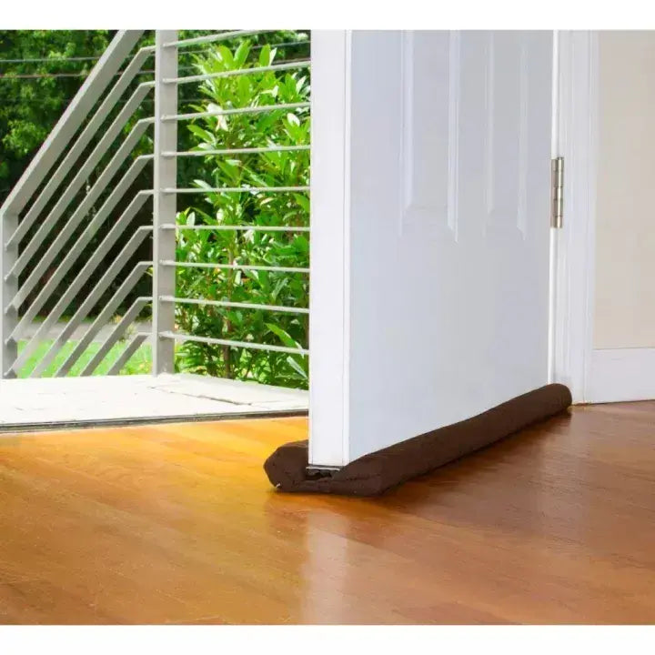 Door draft excluder on a wooden floor with a garden view outside.